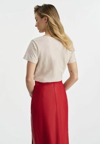 Beżowa koszula z krótkim rękawem o luźnym kroju, połączona z czerwoną skórzaną spódnicą o wysokim stanie, podkreślająca gładkie tekstury i czyste linie.