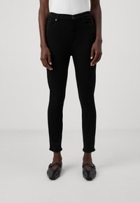 Black slim-fit jeans with a mid-rise waist, five pockets, and a smooth texture. Worn with black flat shoes, featuring a square toe.