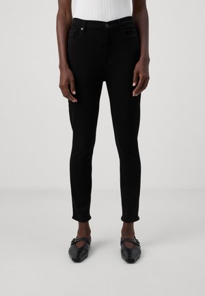 Črne slim-fit kavbojke s srednjim pasom, petimi žepi in gladko teksturo. Ustrezajo črnimi ravnimi čevlji s kvadratnim nosom.