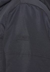 Tessuto giacca navy con una texture liscia, caratterizzato da una piccola patch del logo CMP nera cucita sulla manica superiore.