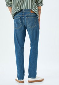 Jeans in denim azzurro chiaro con taglio dritto, caratterizzati da un classico design a cinque tasche. Indossati con sneakers bianche e una camicia a righe verdi.