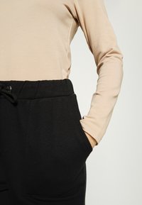 NA-KD PAMELA REIF x NA-KD - TRACKSUIT BOTTOMS - Calças de fato de treino - black