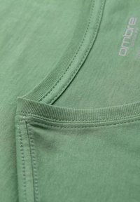 T-shirt in cotone verde con collo rotondo, caratterizzato da una texture liscia e cuciture rinforzate lungo il colletto e l'orlo.