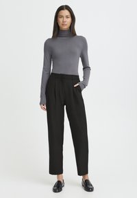 Pull à col roulé gris associé à un pantalon noir taille haute et des mocassins noirs. La tenue présente une coupe ajustée et une coupe droite au niveau des jambes.