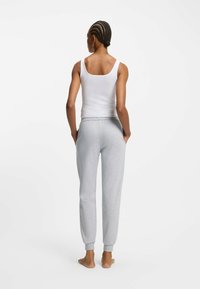 Weißes Tanktop kombiniert mit hellgrauen Jogginghosen. Die Jogginghosen haben einen elastischen Bund und schmale Bündchen. Einfaches Design, weicher Stoff.