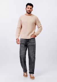 Pull à mailles en beige clair, jeans gris foncé et baskets marron avec des lacets blancs. Design simple, coupe décontractée, détails de texture visibles.