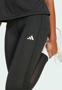 Leggings de sport noirs en tissu extensible, avec une finition texturée, des accents de logo blancs et des panneaux en maille sur les côtés.