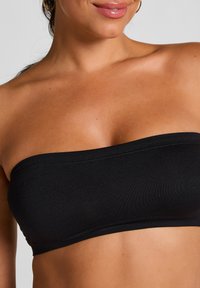 Zwarte strapless bandeau top van glad, rekbaar materiaal met een nette stiksel langs de randen, ontworpen voor een naadloze pasvorm.