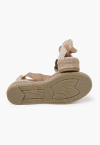 Sandalini espadrillas beige con suola in juta testurizzata, cinturini in tessuto e un fiocco decorativo alla caviglia. Suola piatta per una maggiore facilità d'uso.