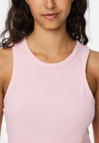 Top de tirantes finos de color rosa claro con cuello redondo, que presenta una textura suave y un diseño ajustado.