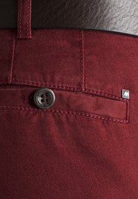 Burgunderfarbene Baumwollhose mit glatter Textur, ausgestattet mit einem Metallknopf und einem kleinen Logotag. Detaillierte Naht entlang der Kanten.