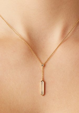 Goldene Halskette mit einem geometrischen Anhänger und einem klaren, länglichen Kristall. Zarte Kette verbindet sich in der Mitte mit einem kleinen Akzent.