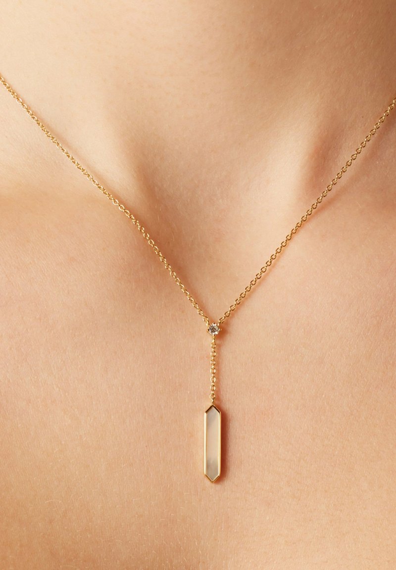 Goldene Halskette mit einem geometrischen Anhänger und einem klaren, länglichen Kristall. Zarte Kette verbindet sich in der Mitte mit einem kleinen Akzent.