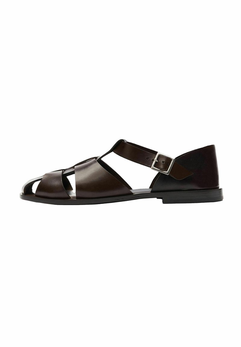 Sandali in pelle marrone con design open-toe, caratterizzati da ampie cinghie incrociate, una cinghia alla caviglia con fibbia in metallo e suola piatta.