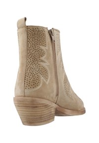 Las botas de tobillo de ante beige presentan un diseño floral perforado, un cierre lateral con cremallera y un tacón de madera apilada para añadir textura y detalle.