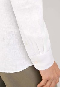 Manga de camisa de lino blanco con cierre de botón, con una sutil textura y detalle plisado. Tejido suave. El dobladillo ligeramente curvado.