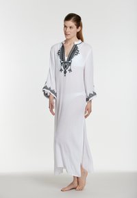 Valge kaftan, millel on mustad tikitud detailid, laiad varrukad ja sügav V-kaelus. Kerge kangas, mille külgedel on lõhkised.