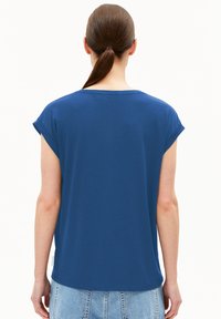 Chemise bleue à manches courtes avec un col rond et des manches retroussées, faite d'un tissu doux. Elle présente un ourlet arrondi et une petite étiquette sur le côté.