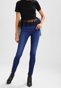 Svart kortärmad topp med genomskinlig tulekant, i kombination med mörkblå tajta jeans och svarta ankelboots. Enkelt mönster och slät textur.