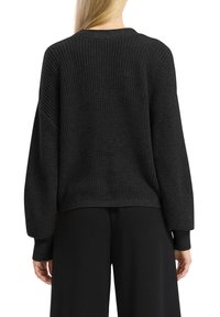 Pull en tricot noir avec une coupe décontractée, doté d'un col rond, de manches tombantes et de poignets côtelés. La texture est épaisse et chaleureuse.