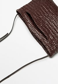 Borsa in pelle intrecciata di colore marrone scuro, forma rettangolare con una superficie liscia, caratterizzata da una cinghia stretta e un design aperto in cima.