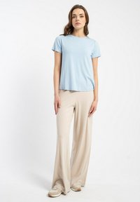 Jasnoniebieska koszulka z krótkim rękawem i beżowe spodnie o szerokich nogawkach. Gładki materiał w luźnym kroju, połączony z jasnymi trampkami.