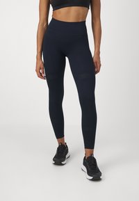 Leggings de cintura alta em azul-marinho com padrão texturizado e design elegante, combinados com sapatilhas de desporto pretas, exibindo uma silhueta ajustada.