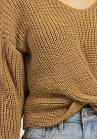 Pull en tricot de couleur beige chaud avec un motif texturé et un décolleté en V, associé à un short en denim bleu clair.