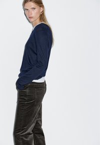 Maglione navy a girocollo con maniche lunghe, abbinato a pantaloni in velluto a coste scuri. Tessuto morbido, vestibilità rilassata e dettagli di cucitura visibili.