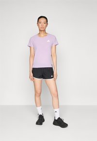 Paarse sport t-shirt met korte mouwen en een mesh ontwerp, met een wit logo, gecombineerd met zwarte sport shorts en zwarte sneakers. Witte crew sokken.