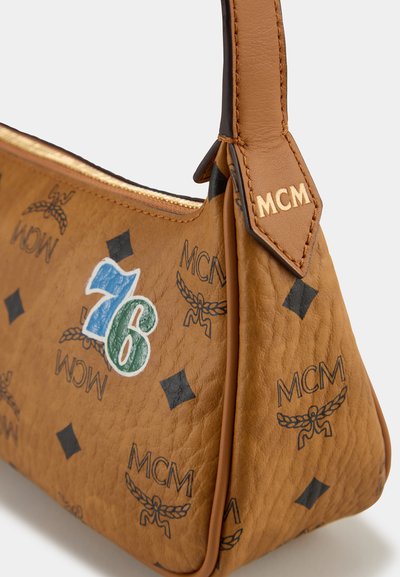 Ruskea nahkainen olkalaukku, jossa on teksturoitu pinta, mustat MCM-logot, sininen ja vihreä numero-patch sekä vaalea hihna.