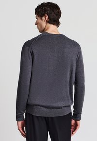 Felpa crewneck grigia scura con un tessuto testurizzato, polsini e orlo a coste, e una vestibilità rilassata. Nessun logo o motivo prominente visibile.