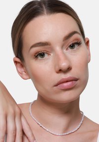 Biała koralikowa naszyjnik choker z owalnymi koralikami, gładką teksturą, lekko przezroczysty, noszony na neutralnym tle w pobliżu szyi osoby.