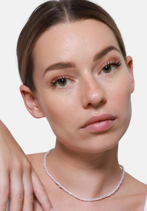 Weißes Perlen-Choker-Halsband mit ovalen Perlen, glatter Textur, leicht transparent, an einem neutralen Hintergrund nahe am Hals einer Person getragen.