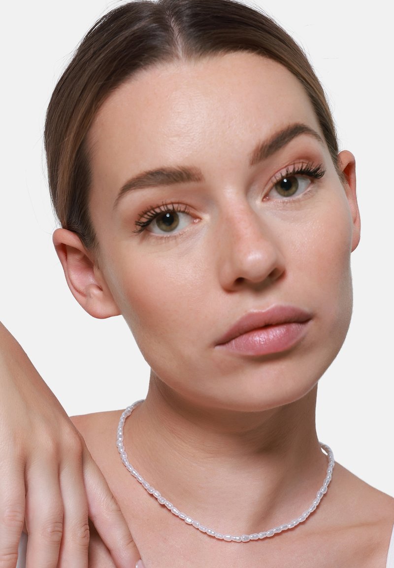 Biała koralikowa naszyjnik choker z owalnymi koralikami, gładką teksturą, lekko przezroczysty, noszony na neutralnym tle w pobliżu szyi osoby.