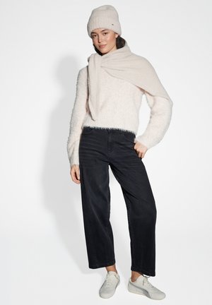 Hellrosa, flauschiger Pullover, schwarze weit geschnittene Jeans, cremige Strickmütze und weiße Turnschuhe. Das Outfit hat strukturierte und geschichtete Details.