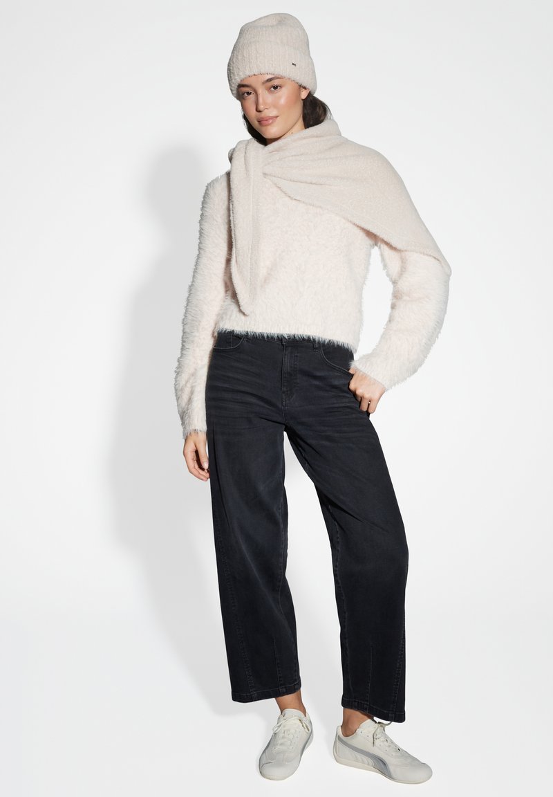 Maglione fluffy rosa chiaro, jeans neri a gamba larga, berretto di maglia crema e sneakers bianche. L'outfit presenta dettagli testurizzati e strati.