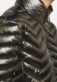 Pufferjakke i mørkegrøn med en chevron-quiltet design, blank finish, høj krave og en synlig lynlås med metalhardware.