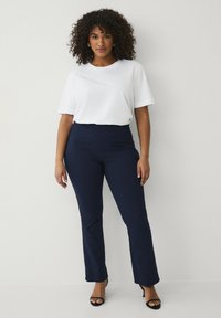 Witte T-shirt met korte mouwen, gecombineerd met strak zittende marineblauwe rechte broek. Gemaakt met zwarte sandalen met straps en hakken. Glad materiaal, geen patronen.