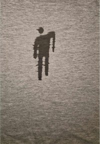 Camiseta de tela gris con una tenue silueta en sombra negra de una persona, que lleva una gorra y tiene un brazo extendido, sobre un fondo texturizado.