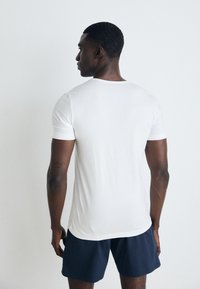 T-shirt blanche à manches courtes en tissu doux, silhouette ajustée et encolure arrondie. Portée avec un short marine, affichant un design simple.