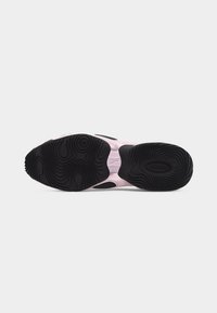Sole of a pink sneaker with black patterned rubber grip, showing textured circular and wavy designs for traction.
