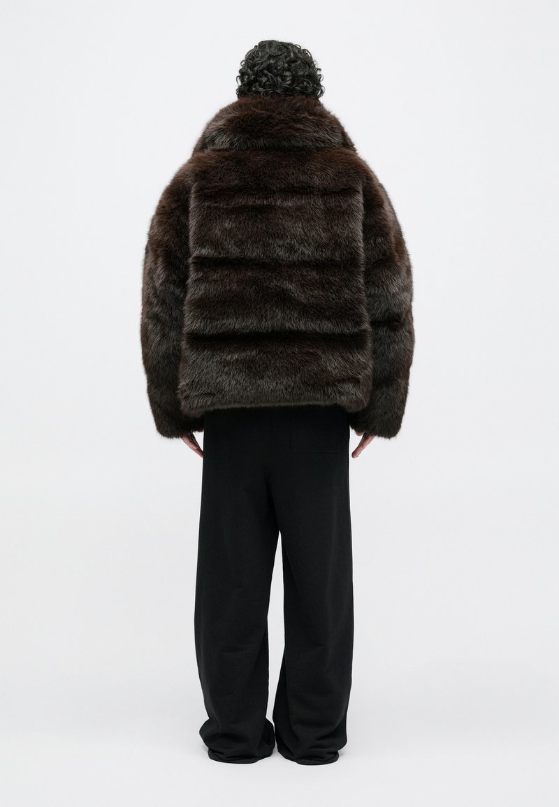 Brown fur coat with a boxy shape and high collar, featuring a textured, layered design. Worn over loose black trousers.