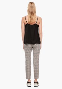 Svart ärmlös topp, texturerat tyg; rutiga byxor i beige, brunt och svart; tillsammans med svarta och vita sneakers.