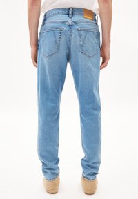 Jean en denim bleu clair avec une coupe droite, comportant deux poches arrière et une étiquette en cuir beige à la taille. Texture douce.