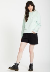 Felpa leggera color menta con coulisse, impreziosita da testo nero. Abbinata a pantaloni shorts in denim neri e stivali neri con accenti gialli.