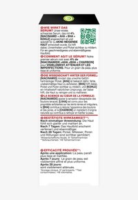 Svart serumförpackning med vit text på tyska och franska, som visar ingredienser och bruksanvisningar. Innehåller QR-kod och information om texturen.