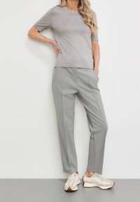 Šedý krátký rukáv top spárovaný se světle šedými kalhotami s kostkovaným vzorem a béžovými teniskami s hnědými akcenty. Jednoduchý, upravený design.