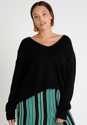 Black knitted oversized sweater with a v-neck, featuring long sleeves and a loose fit, paired with a black and green striped skirt.