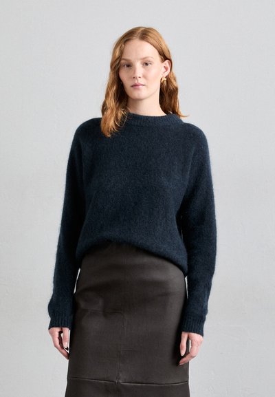 Dunkelblauen, flauschigen Strickpullover mit langen Ärmeln und gerippten Bündchen, kombiniert mit einem taillierten braunen Lederrock. Schlichte runde Ausschnittform.